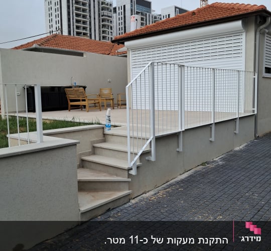 מעקה לבן על מדרגות חיצוניות ליד מבנה עם גג רעפים אדום